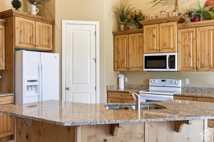 Kitchen featuring wood cabinetry, granite countertops, an undermount double-basin sink, and a white side-by-side refrigerator