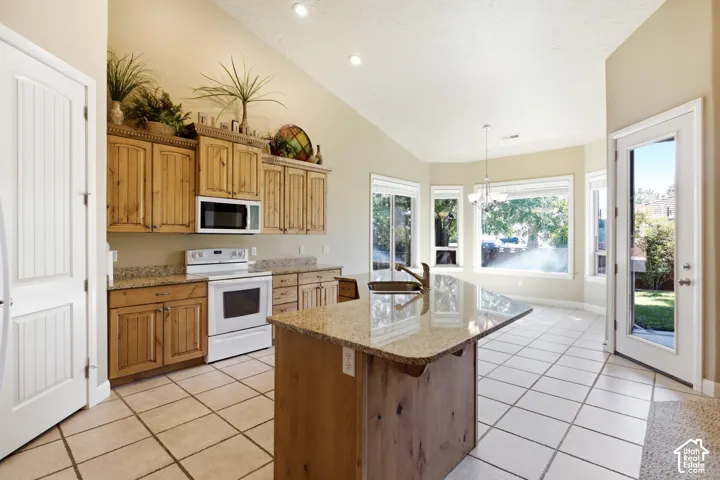 Kitchen featuring a vaulted ceiling, wood cabinetry, granite countertops, a center island with sink, and tile flooring
