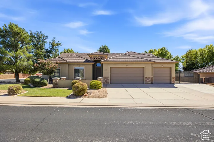 Stucco exterior with stone accents, a tiled roof, a three-car garage, and a wrought iron gate