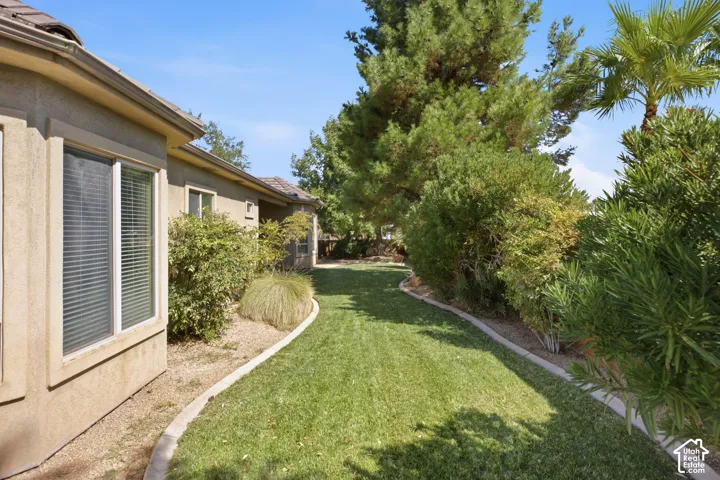Side yard featuring a manicured lawn, established shrubs, and mature trees
