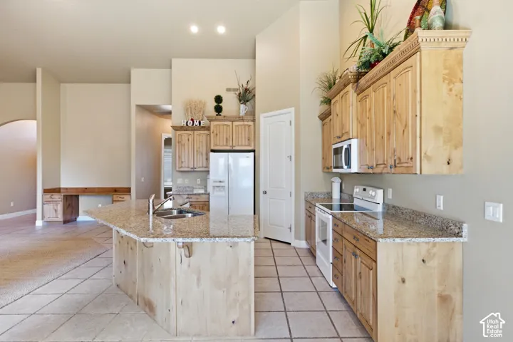 Kitchen featuring wood-finish cabinetry, a built-in microwave, a flat-top electric range, and an island with an undermount sink