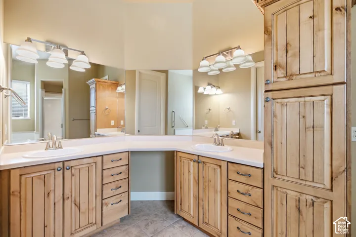 Dual basin vanity with solid surface countertops, natural wood cabinetry, and integrated storage tower