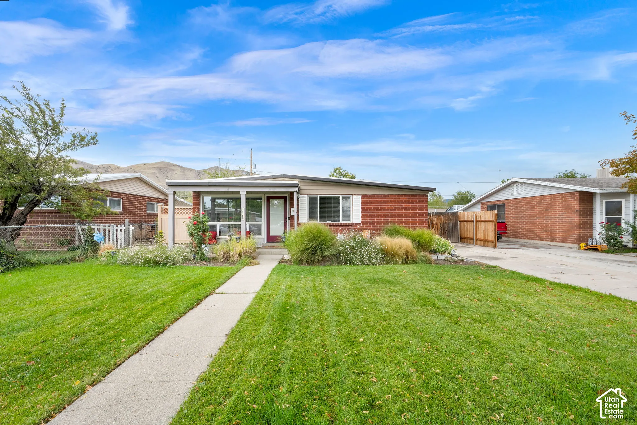 Brick ranch home featuring a manicured front lawn with mature landscaping, concrete walkway, and attached garage