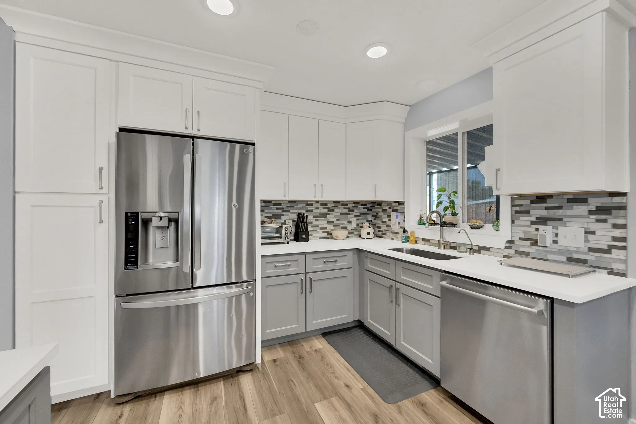 White upper cabinetry, gray lower cabinetry, mosaic tile backsplash, stainless steel appliances, and wood-finish flooring
