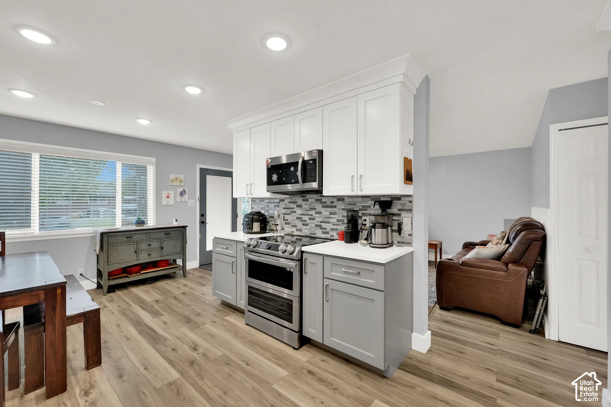 Modern kitchen featuring white upper cabinetry, gray lower cabinetry, stainless steel appliances, wood-finish flooring, and recessed lighting