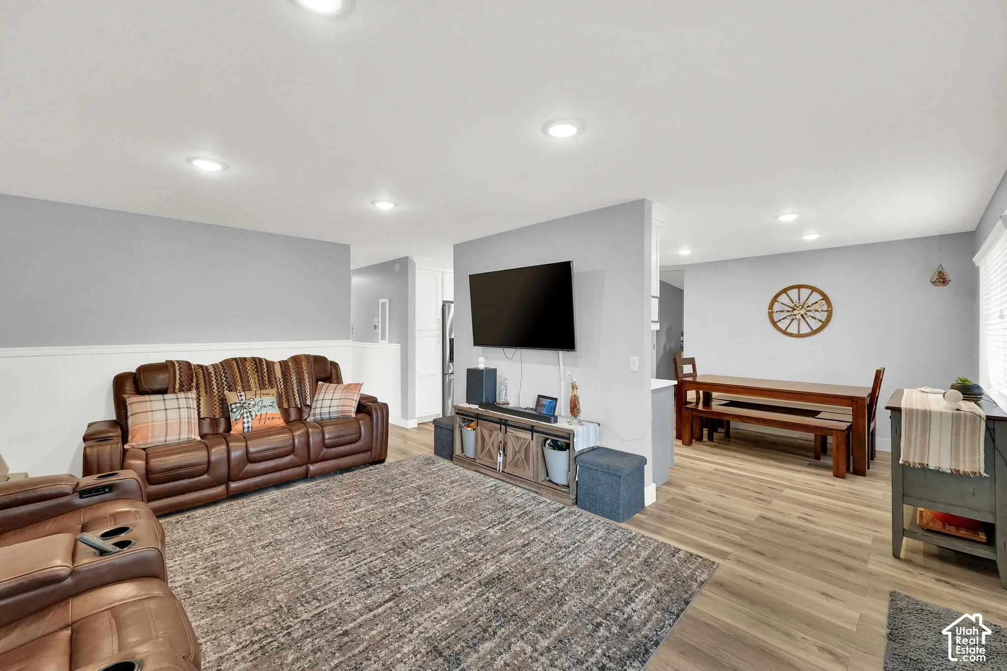 Spacious open-concept living area featuring recessed ceiling lighting, wood-finish flooring throughout, and a neutral color palette with two-tone wall treatment