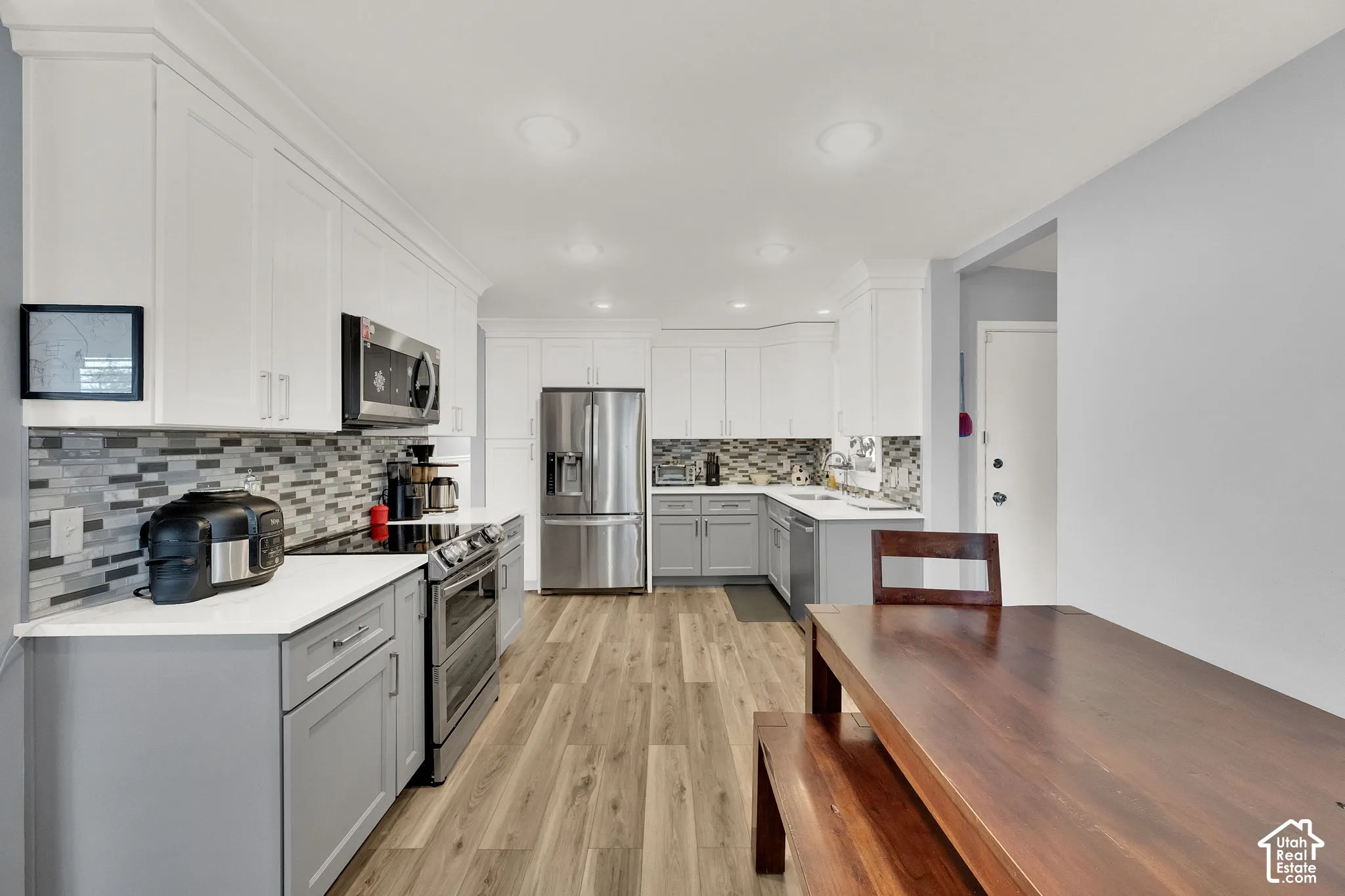 Modern kitchen featuring white upper cabinetry, gray lower cabinetry, stainless steel appliances, and a mosaic tile backsplash