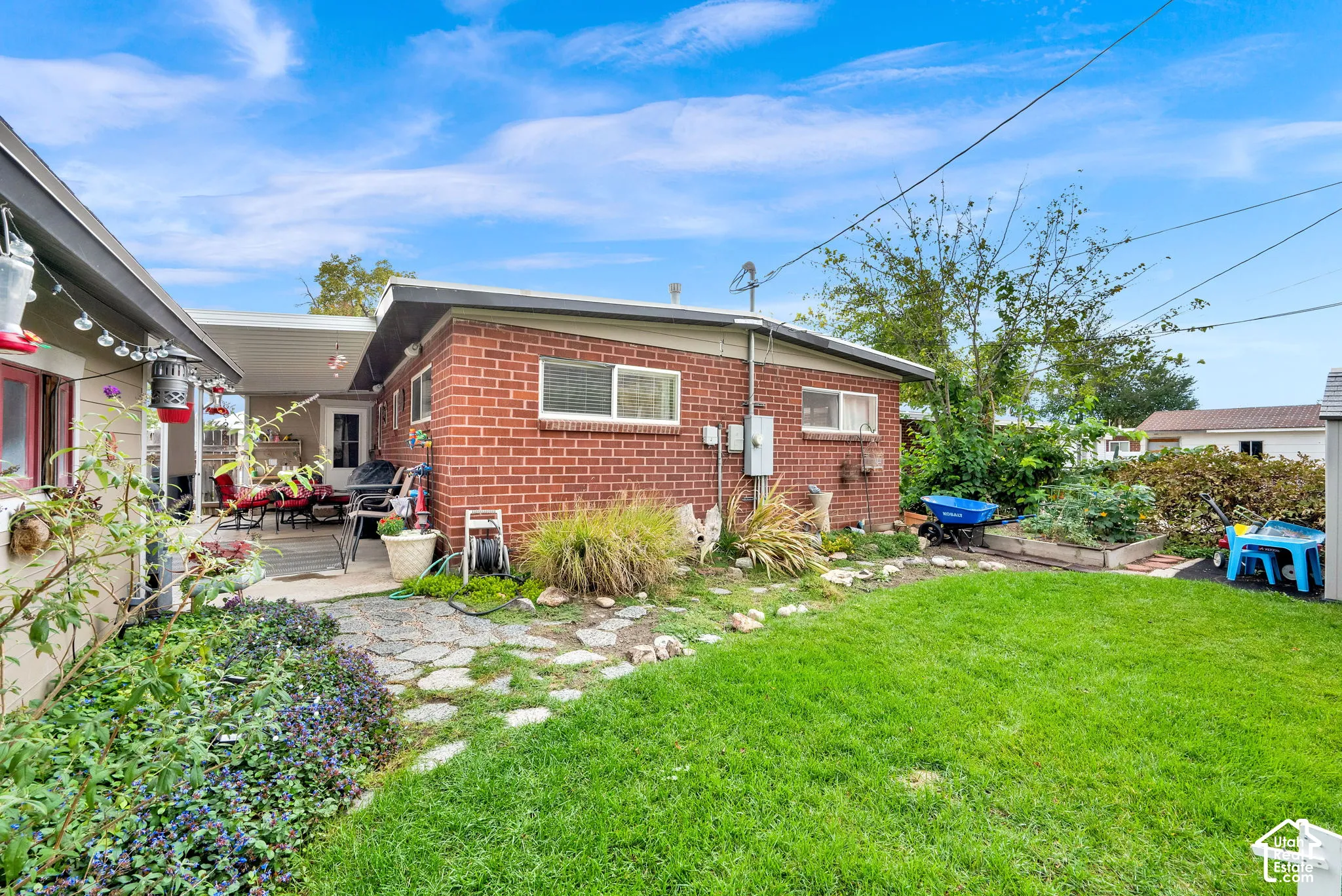 Expansive backyard featuring a covered patio, manicured lawn, stone pathway, and raised garden beds