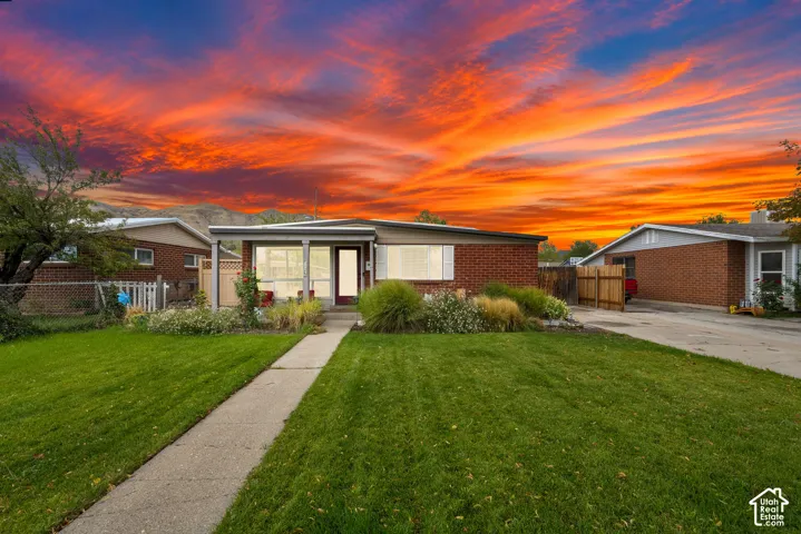 Single-story brick exterior, covered front entry, concrete walkway, established front landscaping, and a driveway with a wooden fence