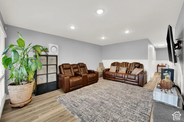 Recessed lighting illuminates the room featuring wood-finish flooring, a wall-mounted television bracket, and a half wall with white paneling