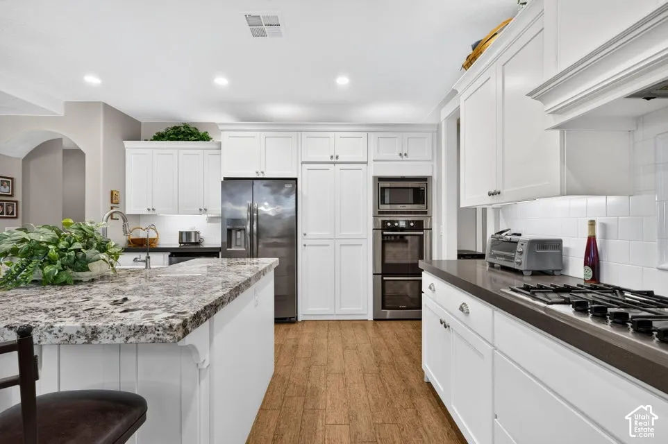 Kitchen featuring wood-finish flooring, white cabinetry, a kitchen island with a stone countertop, a built-in double oven, and a gas cooktop