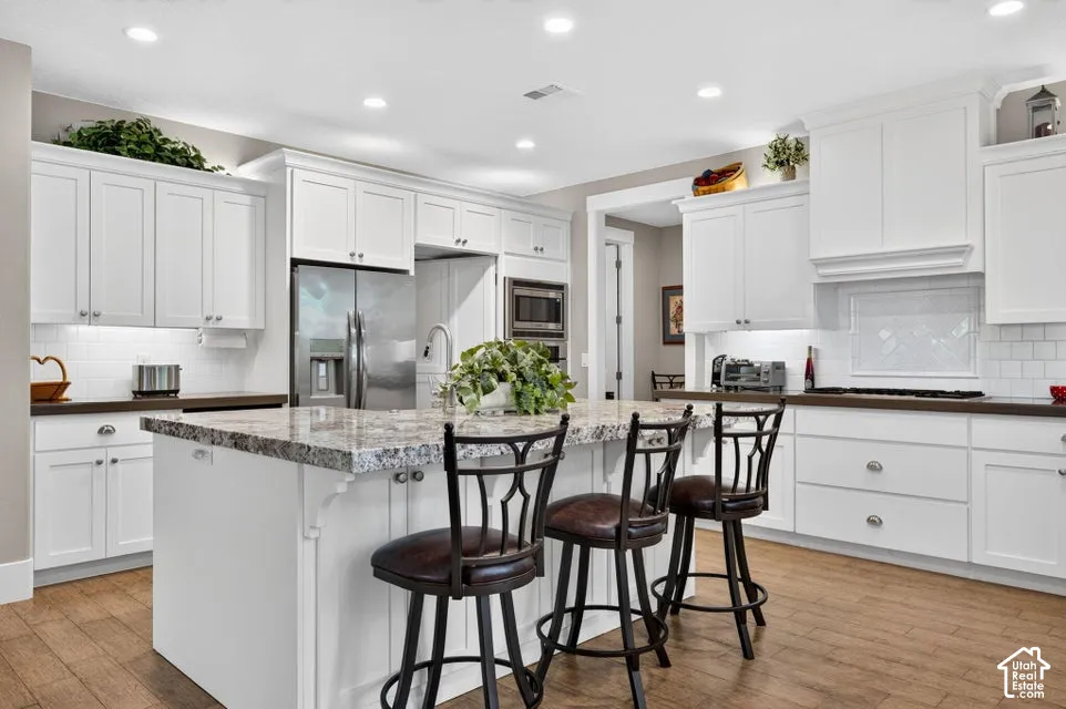 Kitchen featuring white cabinetry, a large center island with stone countertop, stainless steel appliances, wood-finish flooring, and recessed lighting