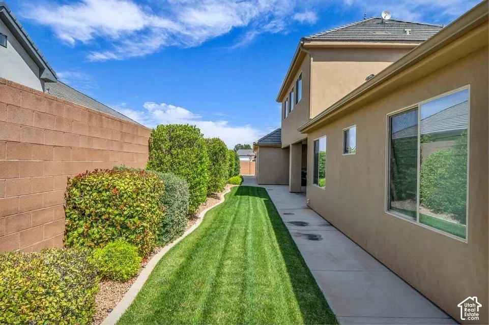 Landscaped side yard featuring a brick perimeter wall, mature shrubbery, and a manicured lawn