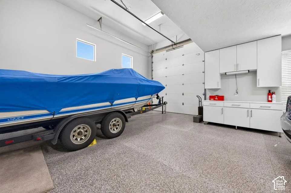 Spacious garage featuring a large overhead door, two high windows, built-in white cabinetry, a built-in countertop, and speckled epoxy flooring