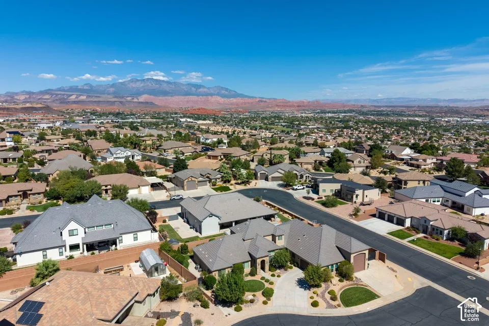 Residential neighborhood with varied architectural styles under a clear sky, featuring distant red rock formations and mountains