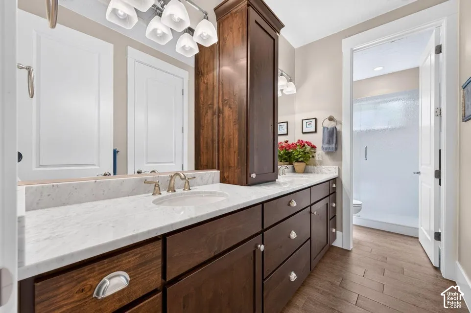 Wood-finish plank flooring, an extended single vanity with an undermount sink, a light-toned countertop, and rich wood cabinetry, with a separate shower enclosure