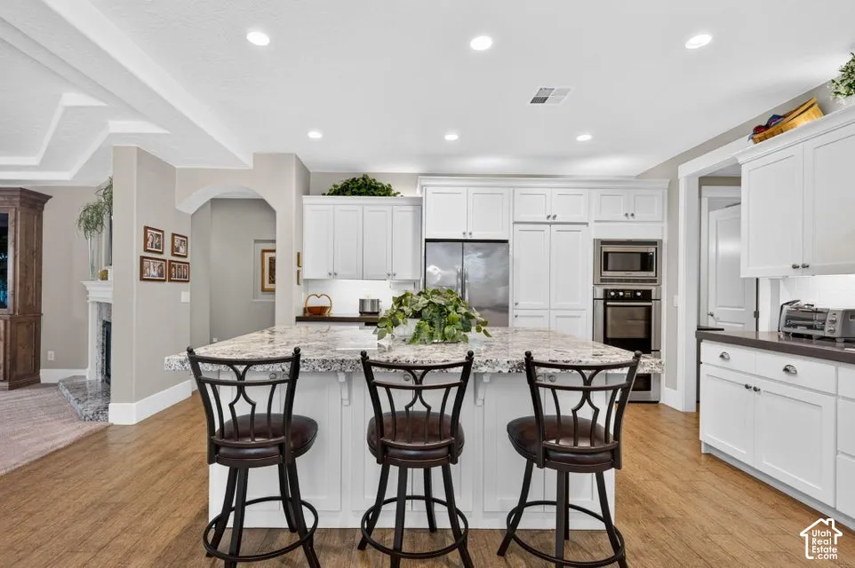 Kitchen featuring a large central island with seating, white cabinetry, integrated stainless steel appliances, recessed lighting, and wood-finish flooring