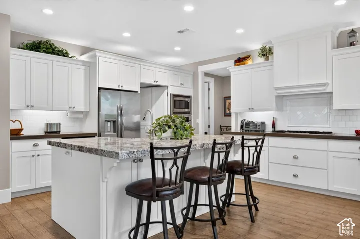Kitchen featuring white cabinetry, a large center island with stone countertop, stainless steel appliances, wood-finish flooring, and recessed lighting