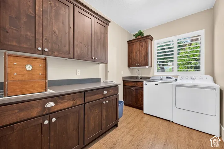 Dark wood-finish cabinetry, light-toned countertops, wood-look flooring, built-in utility sink, and window with plantation shutters