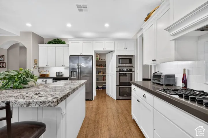 Kitchen featuring white cabinetry, stainless steel appliances, wood-finish flooring, a kitchen island with a stone countertop, and a built-in pantry