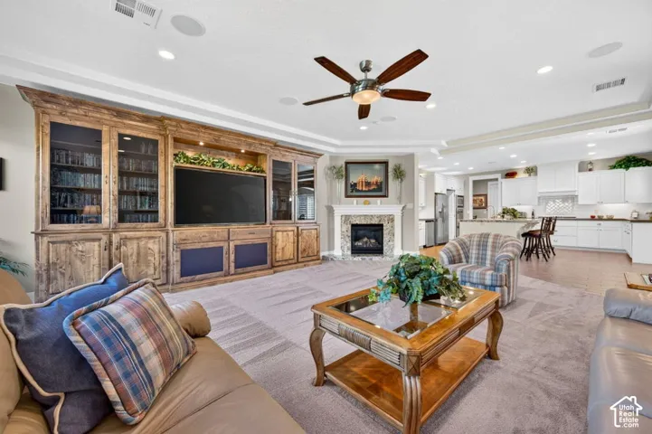 Built-in wood-finish media center, recessed lighting, ceiling fan, corner fireplace with tile surround, and open-concept kitchen with white cabinetry