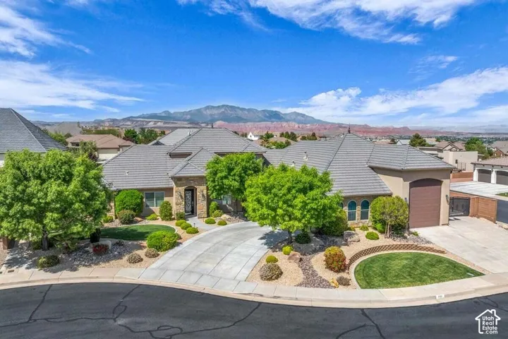 Stucco exterior with stone accents, tile roofing, an attached garage, and a curved driveway