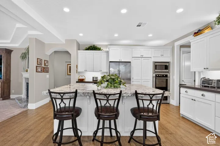 Kitchen featuring a large central island with seating, white cabinetry, integrated stainless steel appliances, recessed lighting, and wood-finish flooring