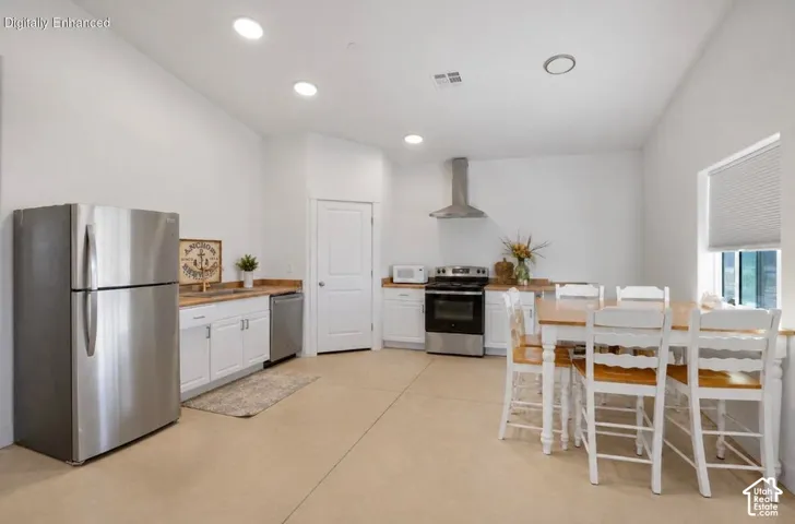 Bright, open kitchen featuring stainless steel appliances, white cabinetry with wood-finish countertops, tile flooring, recessed lighting, and a dedicated dining area with seating for multiple guests