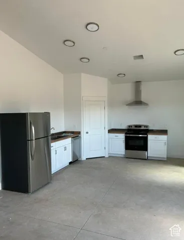 White cabinetry with dark countertops, stainless steel appliances, and concrete flooring