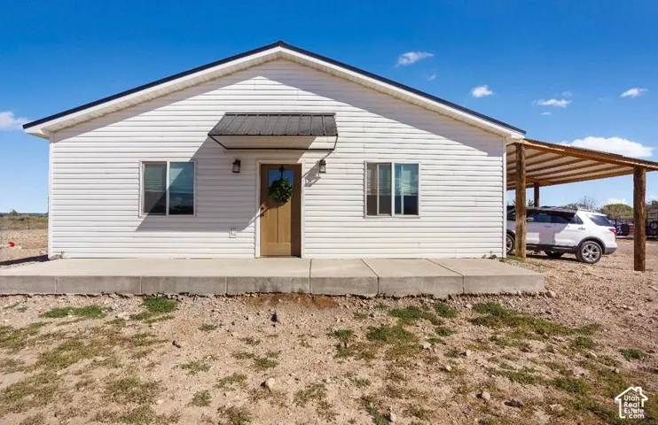 White siding exterior with black trim, wood-finish entry door, and metal awning