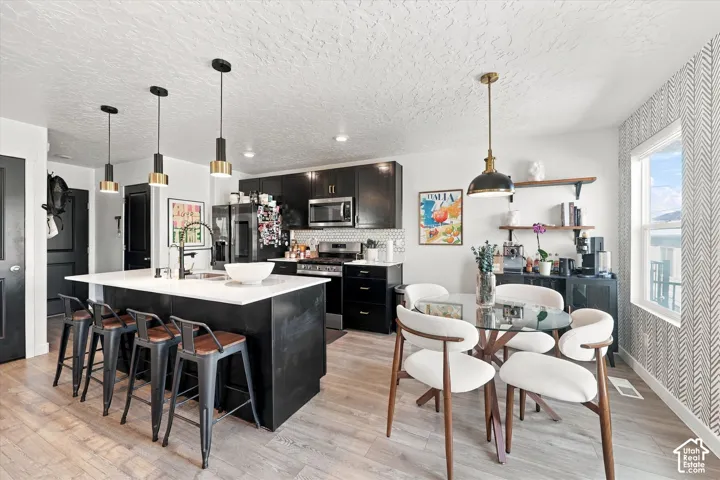 Kitchen featuring an expansive island with seating, dark shaker-style cabinetry, a subway tile backsplash, and stainless steel appliances