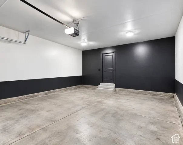 Concrete flooring, dark gray door, overhead lighting, garage door opener mechanism