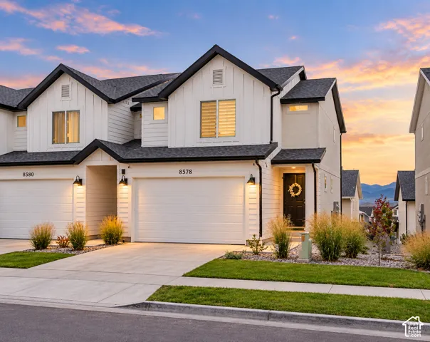 Modern white siding exterior with contrasting black trim, attached two-car garage, concrete driveway, and front entryway with exterior lighting fixtures