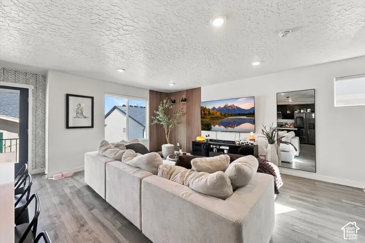 Recessed ceiling lighting, wood-finish flooring, accent wallpaper, a large window, and a built-in wood panel feature wall