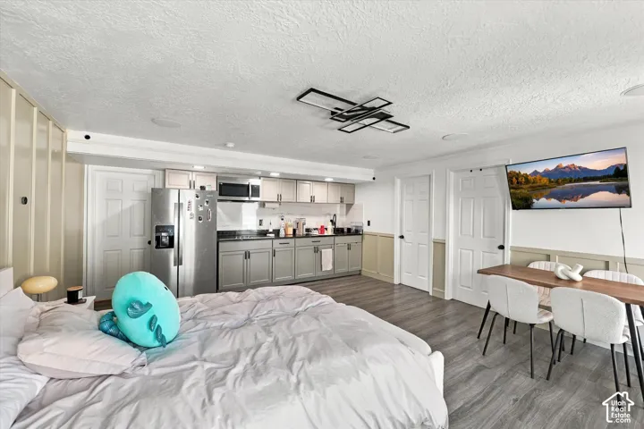 Full kitchen with stainless steel appliances, modern overhead lighting fixture, wood-finish flooring, and panel accent wall