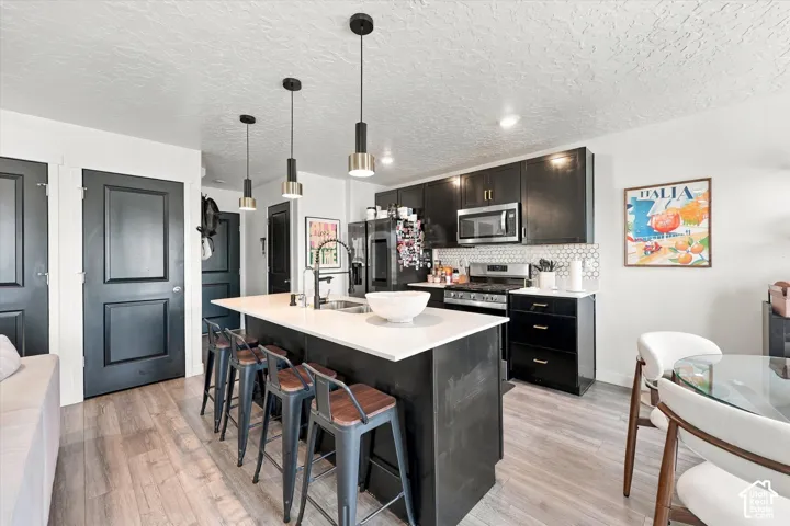 Kitchen featuring a central island with white countertop, black cabinetry, stainless steel appliances, and a white hexagon tile backsplash