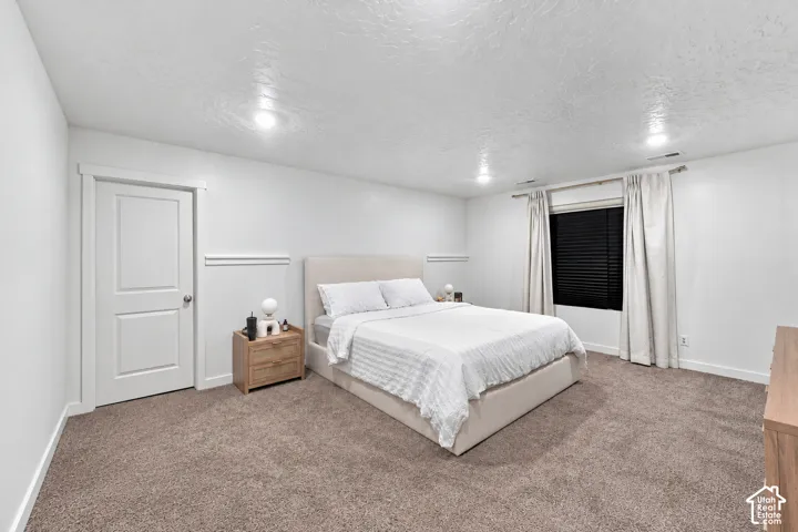 Recessed lighting illuminates the room, featuring a neutral color palette, plush carpeting, and a window with blinds and drapes