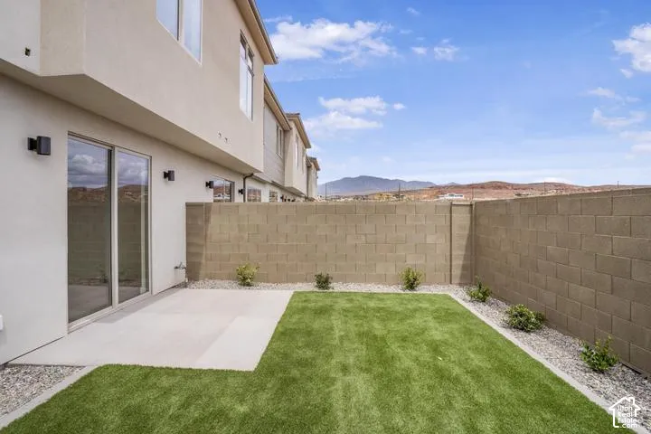 Backyard featuring a concrete patio, artificial turf, a block wall fence, and desert landscaping