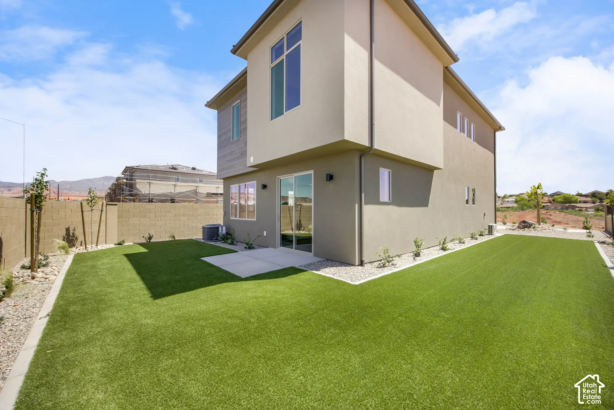 Rear exterior featuring a concrete patio, artificial turf, and a stucco finish