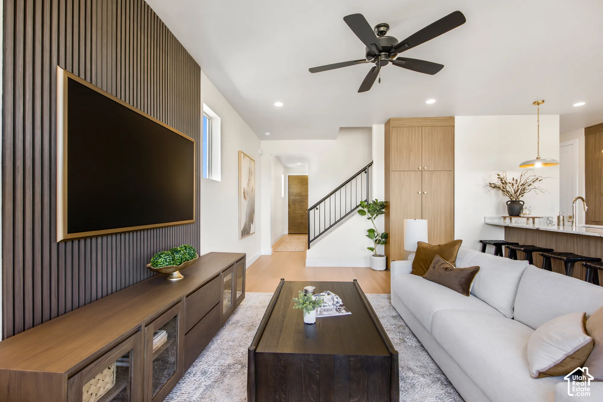 Vertical slatted accent wall, light wood-finish flooring, recessed lighting, ceiling fan, and built-in cabinetry