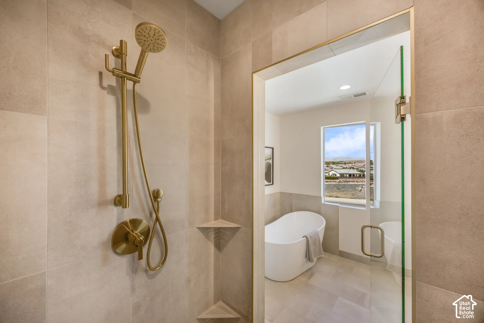 Walk-in shower with gold-finish fixtures and an integrated corner shelf, featuring a freestanding soaking tub and a fixed window