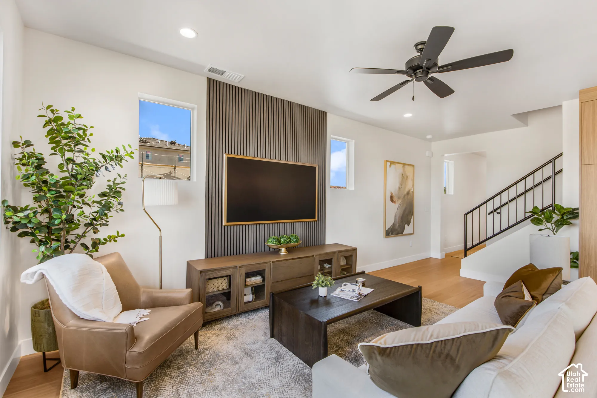 Recessed lighting, wood-finish flooring, accent wall with vertical paneling, contemporary ceiling fan, and staircase with metal railing