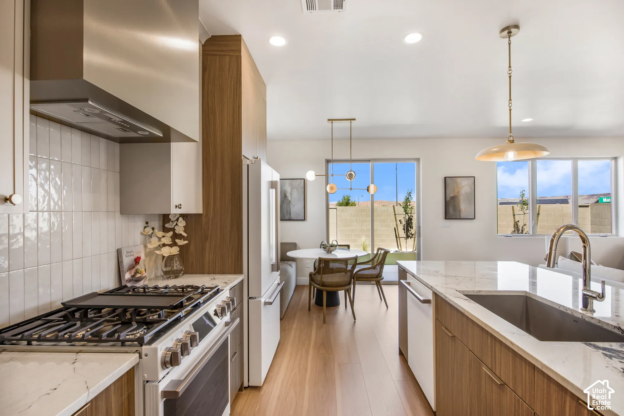 Gourmet kitchen with stainless steel appliances, wood-finish cabinetry, light stone countertops, and a white subway tile backsplash