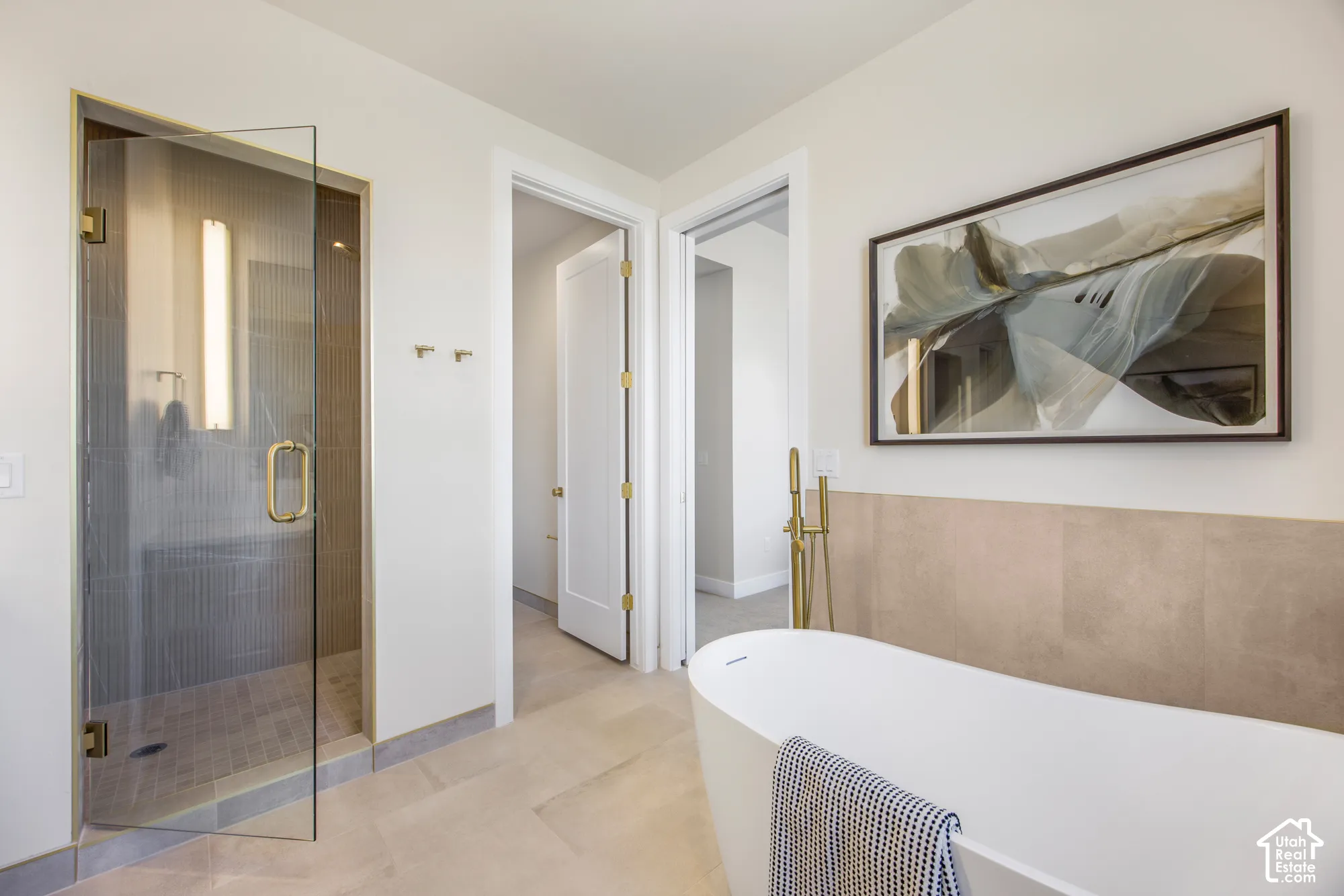 Freestanding soaking tub with floor-mounted brass fixture, glass-enclosed shower with brass hardware, and light-toned tile flooring