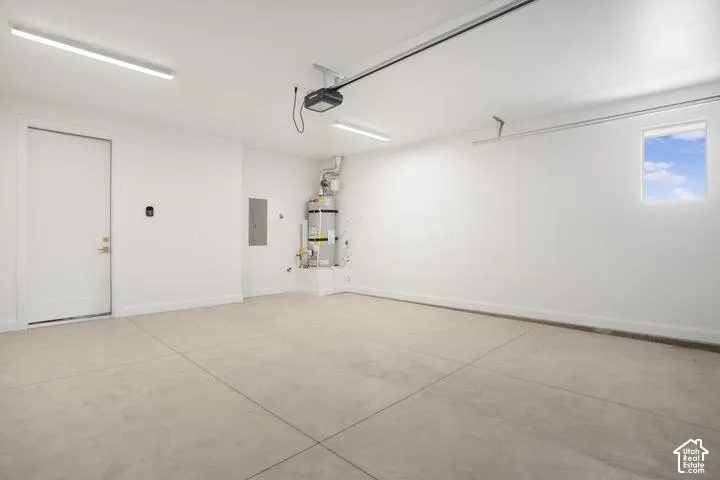 Concrete flooring with an overhead garage door opener, fluorescent lighting, and a water heater