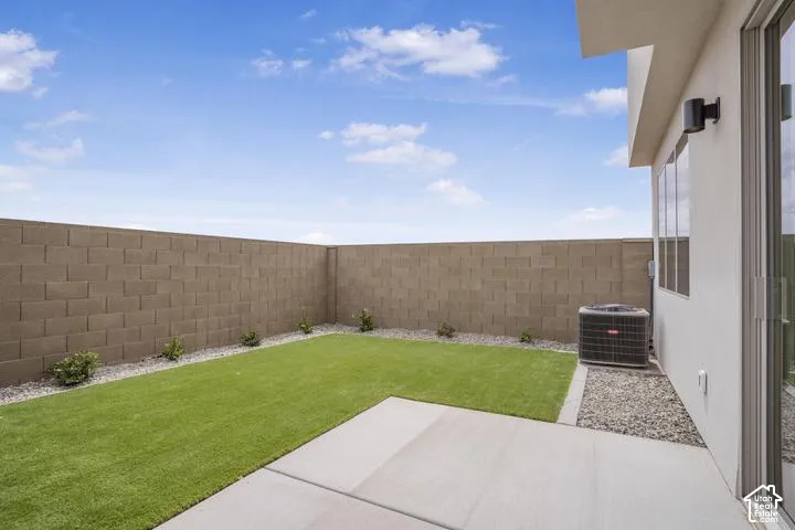 Enclosed backyard featuring a concrete patio, artificial turf, and a block wall