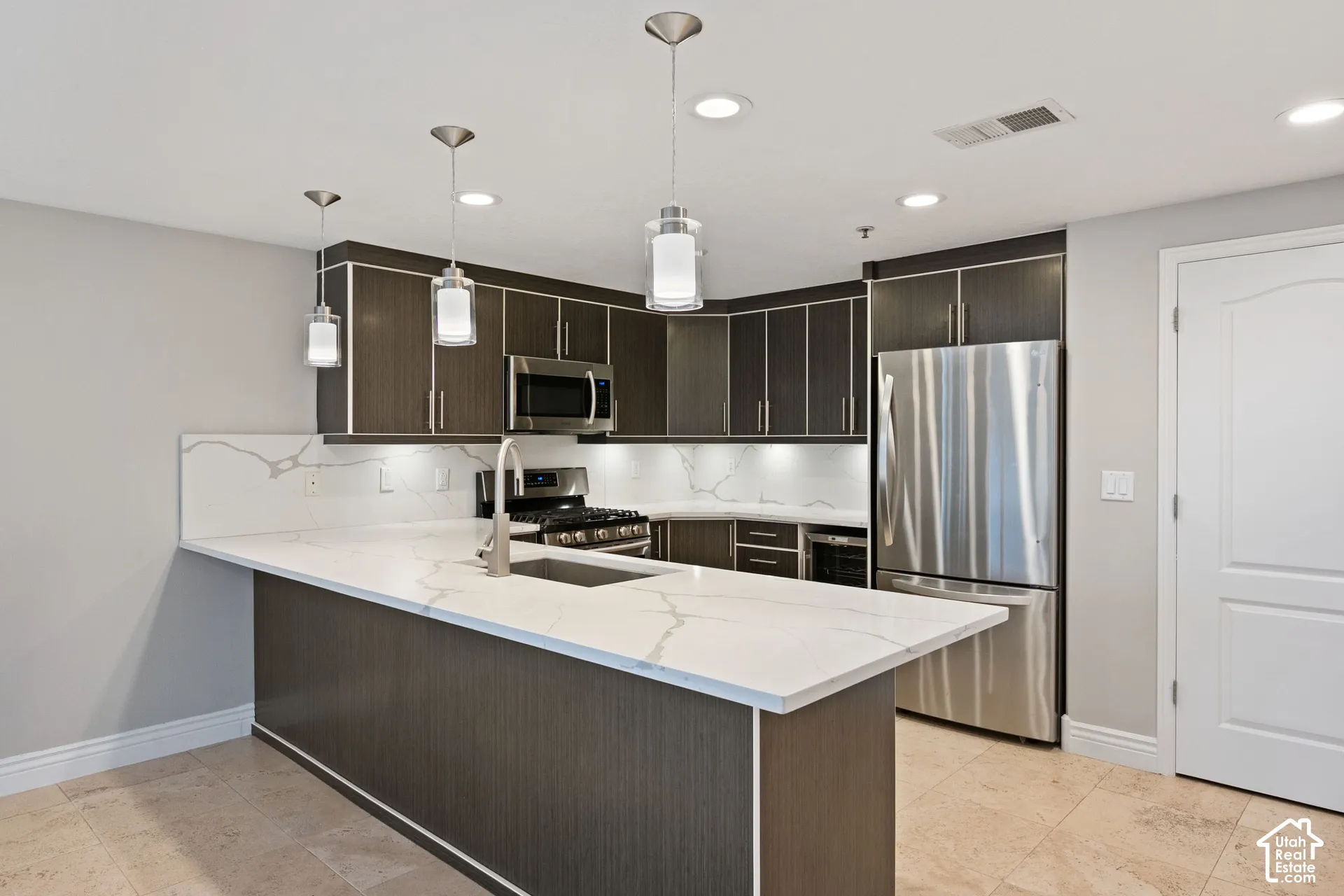 Modern kitchen featuring dark cabinetry with brushed metal hardware, white quartz countertops, and a large waterfall-edge island