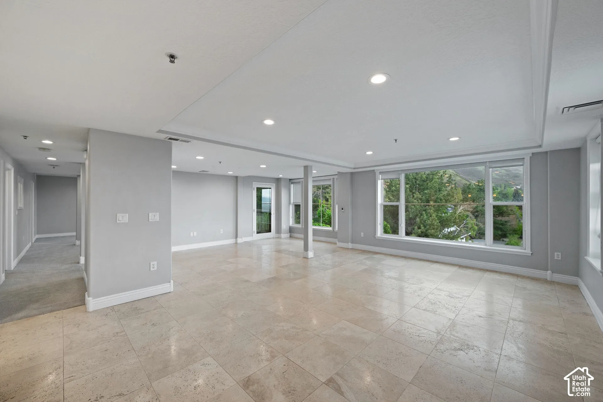 Spacious open-concept room featuring large windows, recessed lighting, crown molding, and tiled flooring
