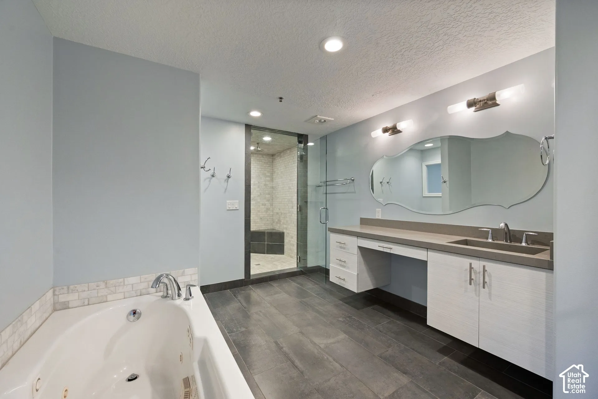 Spacious bath featuring wood-finish flooring, a soaking tub with tile surround, a walk-in shower with glass enclosure, a dual vanity with integrated sink, and an ornate mirror