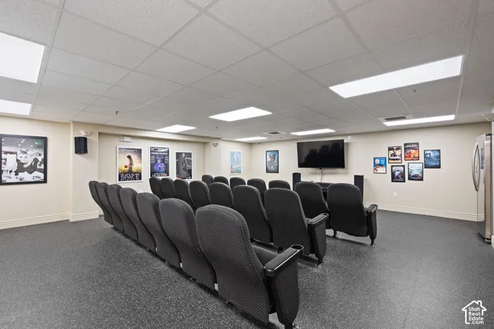 Dedicated media room featuring tiered stadium-style seating with individual black mesh chairs, recessed ceiling lighting, flat-screen display, and neutral carpeted flooring throughout